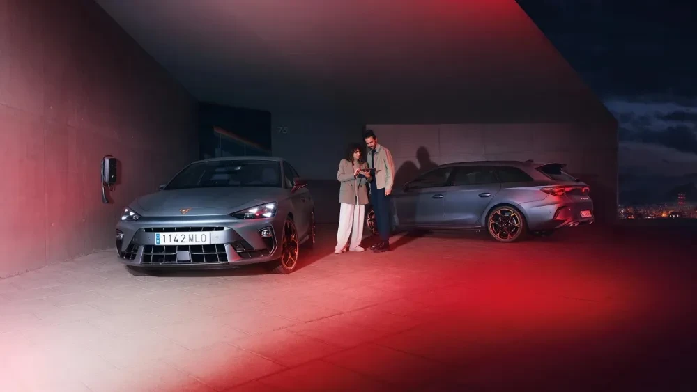 Man en vrouw die op hun telefoon kijken naast 2 CUPRA modellen