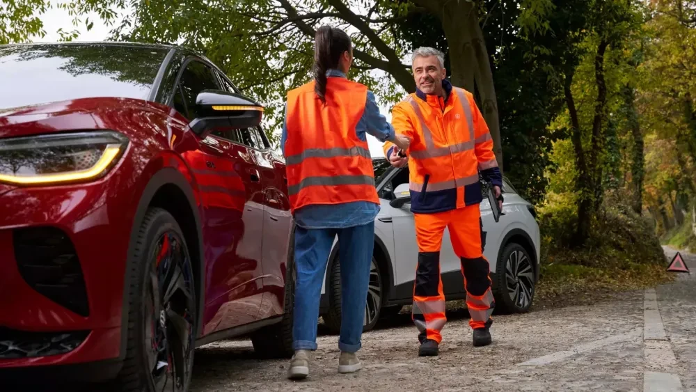 Vrouw met pech en Volkswagen medewerker schudden elkaar de hand naast een auto, ze hebben veiligheidsvestjes aan