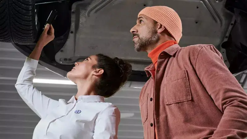 Volkswagen servicemonteur en klant bekijken de onderkant van een auto in de werkplaats