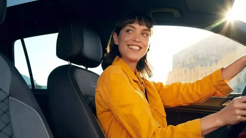 Vrouw zit achter het stuur van een Volkswagen Tiguan en lacht naar iemand buiten